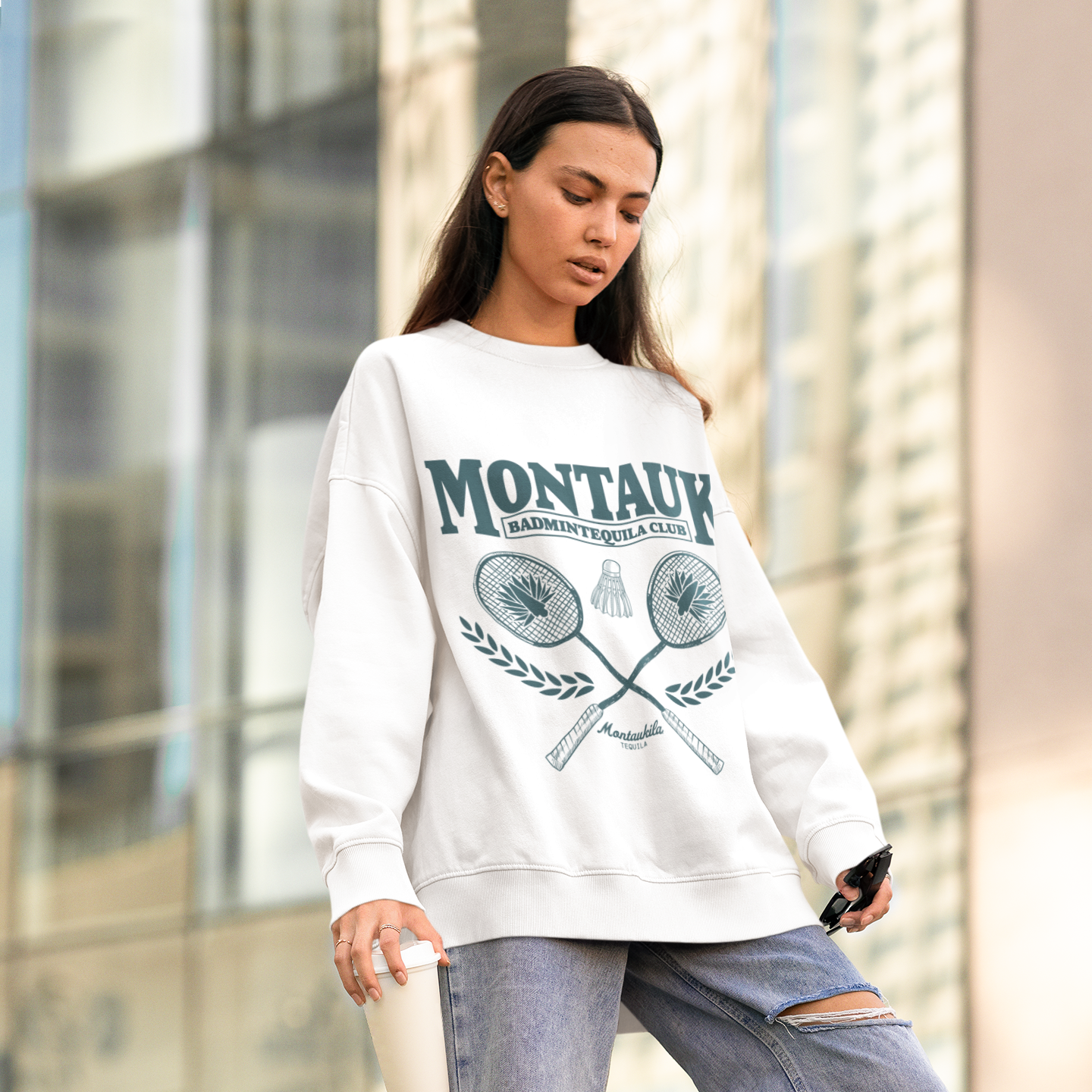 Person wearing a white sweatshirt with 'Montauk' print and ripped jeans in an urban setting.